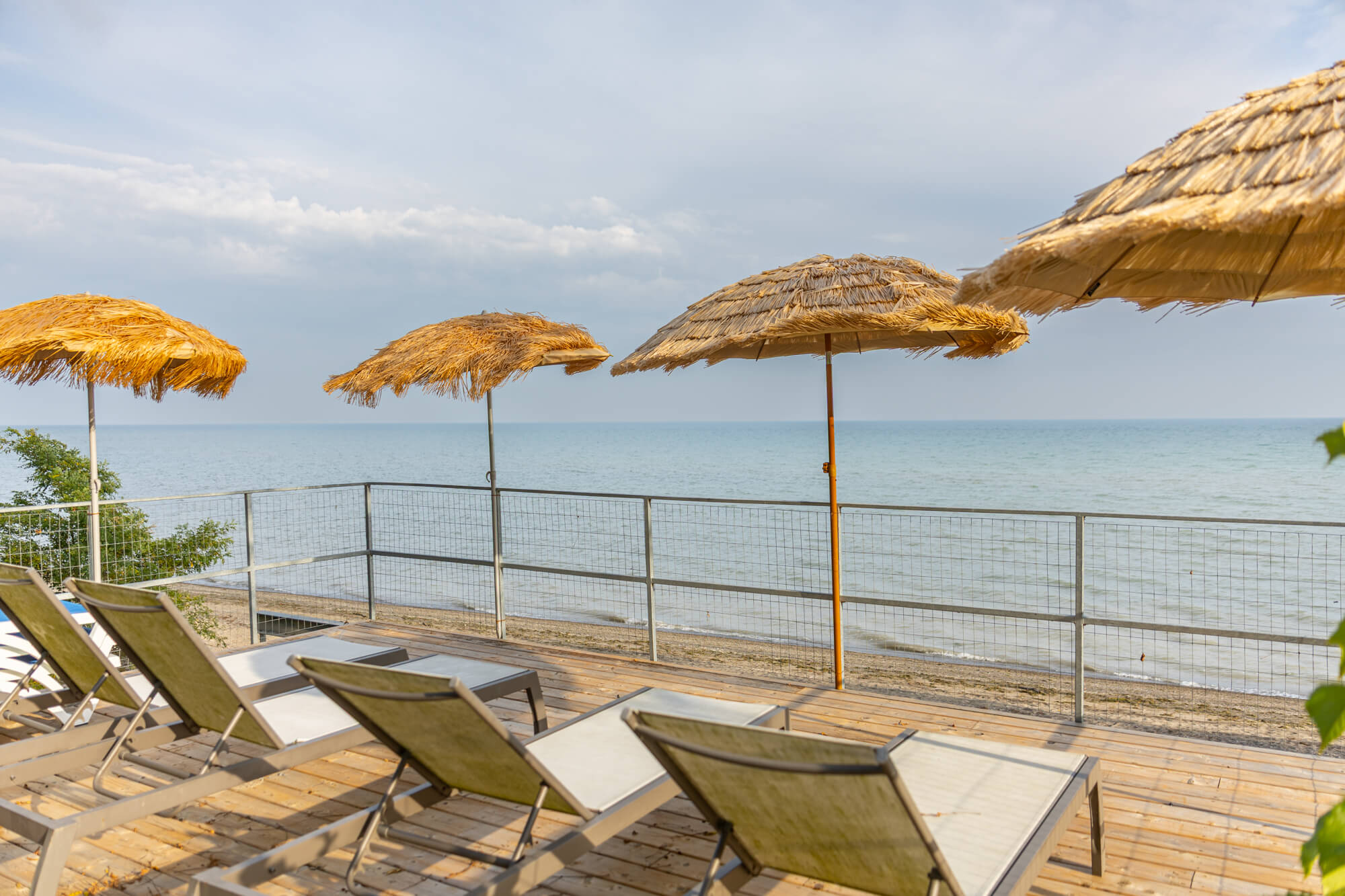 Lakefront deck at Ontario VRBO rental — lounge chairs with tiki straw umbrellas, sandy beach and calm lake water, perfect for summer stays
